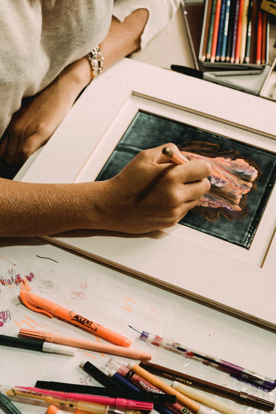 Hand using a tool to create abstract art with orange and purple colors.