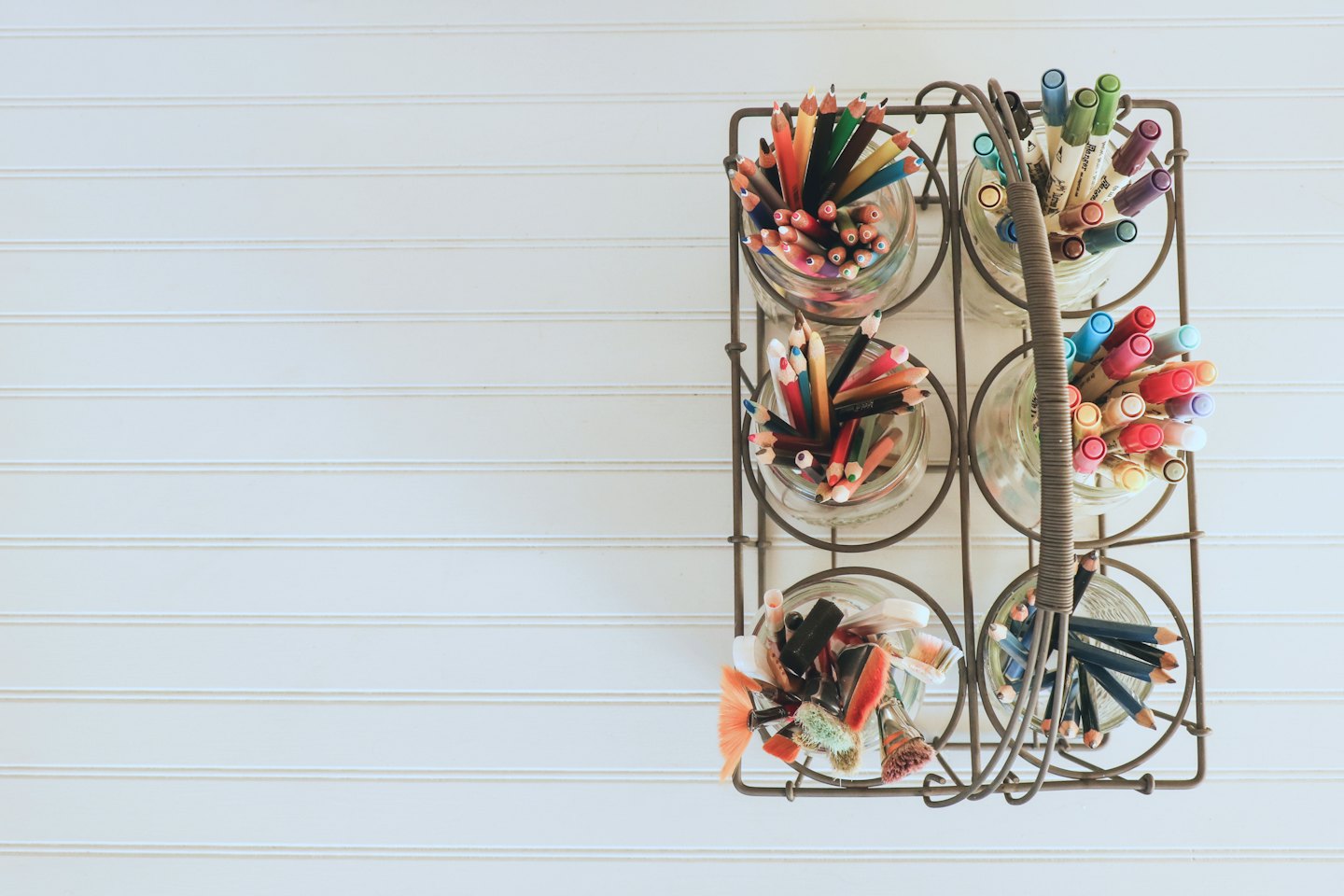 Colored pencils, markers, and paintbrushes stand in jars inside a caddy.