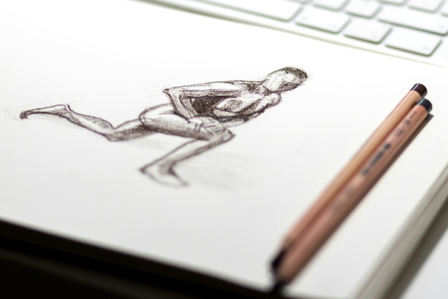 Sketchbook showing charcoal figure sketch with pencils and laptop.